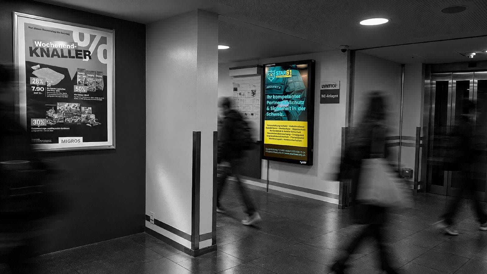 Digitale Werbefläche im Migros Altdorf, daneben ein gedrucktes Plakat